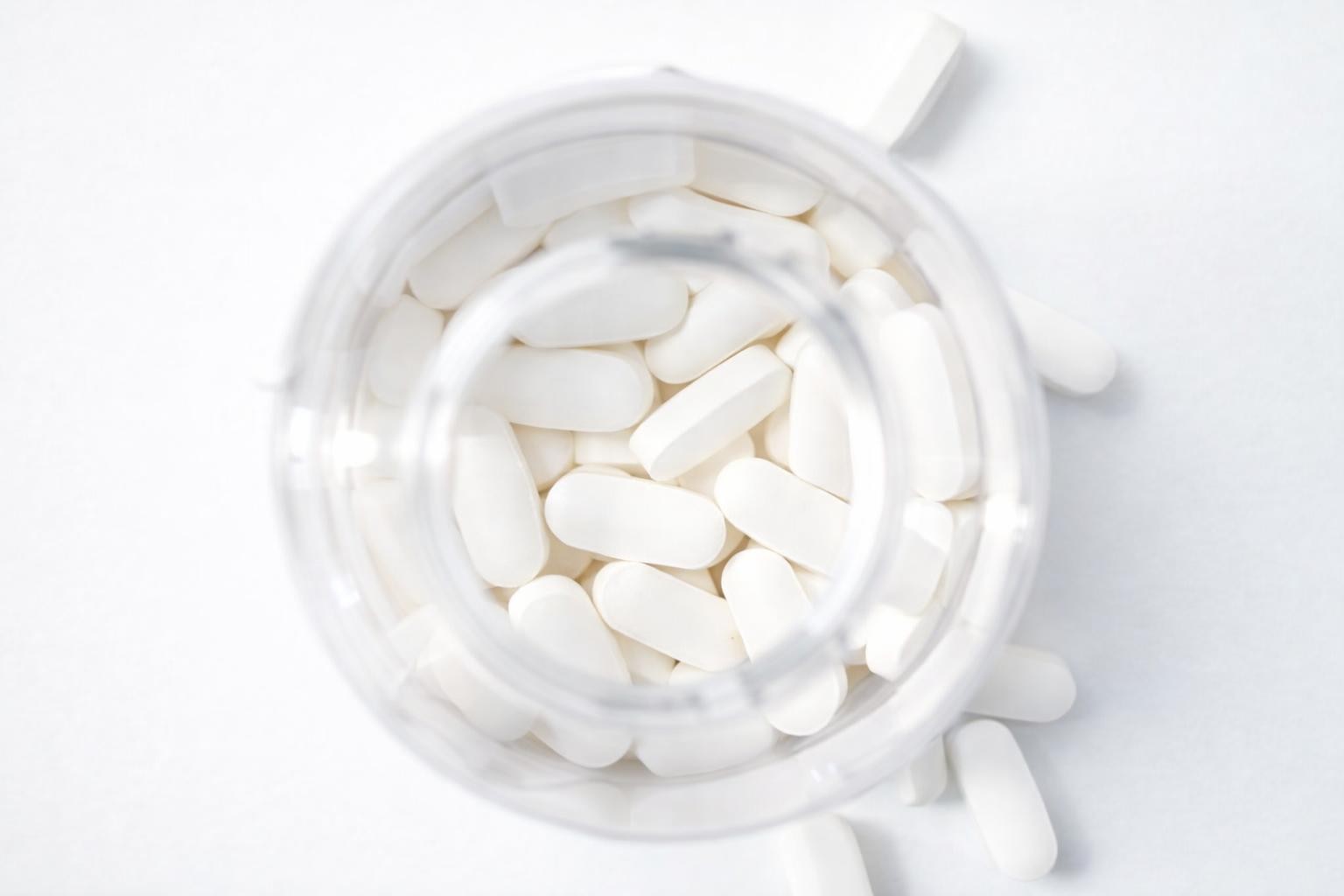 White magnesium tablets viewed from the top of a clear glass jar on a white background.